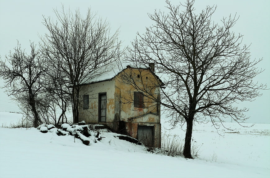Abandoned yellow house in snowy winter landscape with bare trees