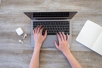 Top view of hands typing on laptop with notebook and earbuds