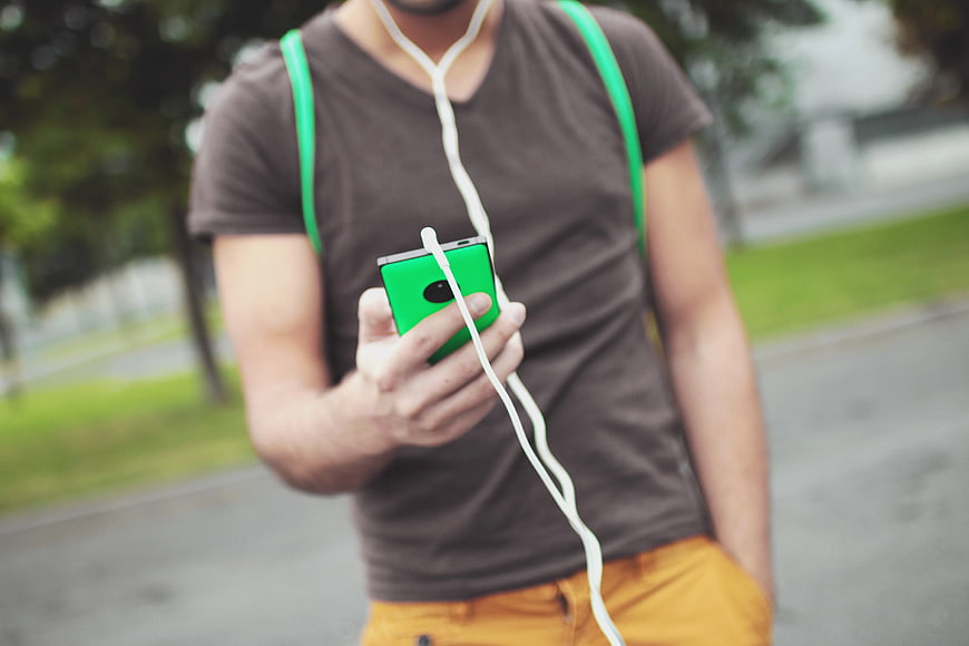 Man with Green Smartphone and White Earphones
