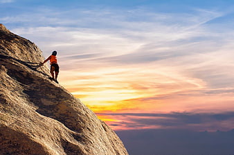 Rock Climber Scaling Mountain Peak at Sunset