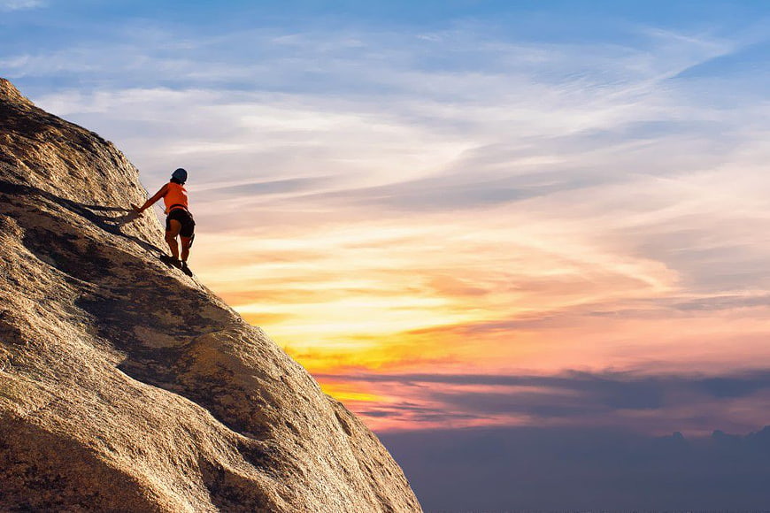 Rock Climber Scaling Mountain Peak at Sunset