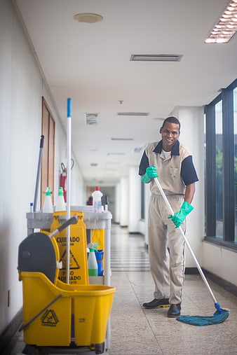 Smiling male janitor mopping hospital corridor with yellow cleaning cart