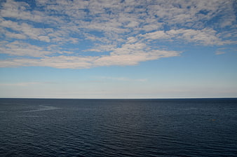 Serene ocean horizon with blue sky and scattered clouds