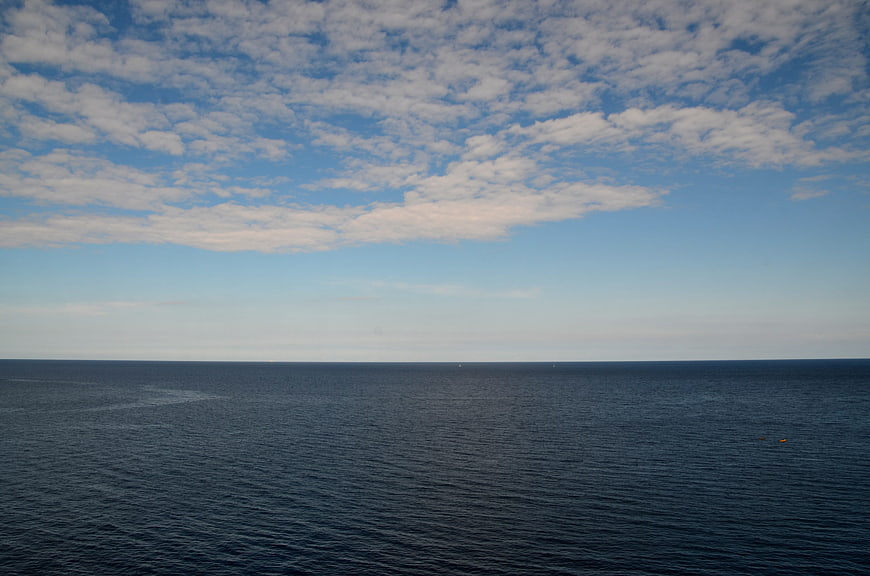 Serene ocean horizon with blue sky and scattered clouds
