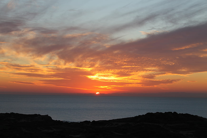 Dramatic orange sunset over ocean with silhouetted rocky foreground