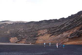 Tourists walking on black volcanic sand beach near crater