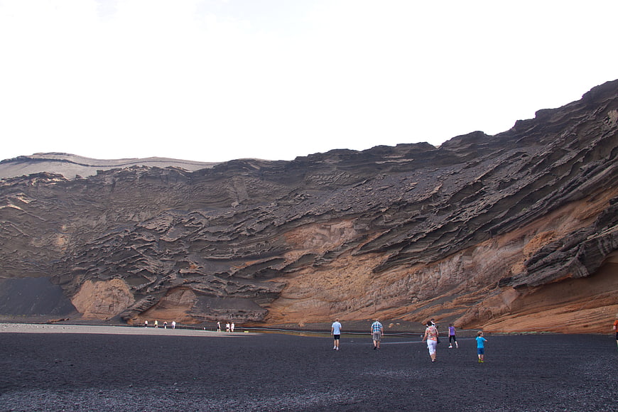 Tourists walking on black volcanic sand beach near crater