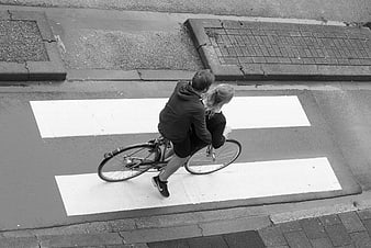 High angle black and white photo of couple on bicycle crossing street