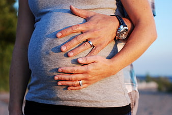 Pregnant woman holding belly with partner's hands outdoors