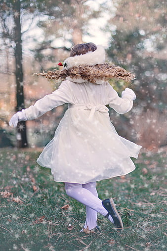 Little girl in white coat twirling in snowy winter forest