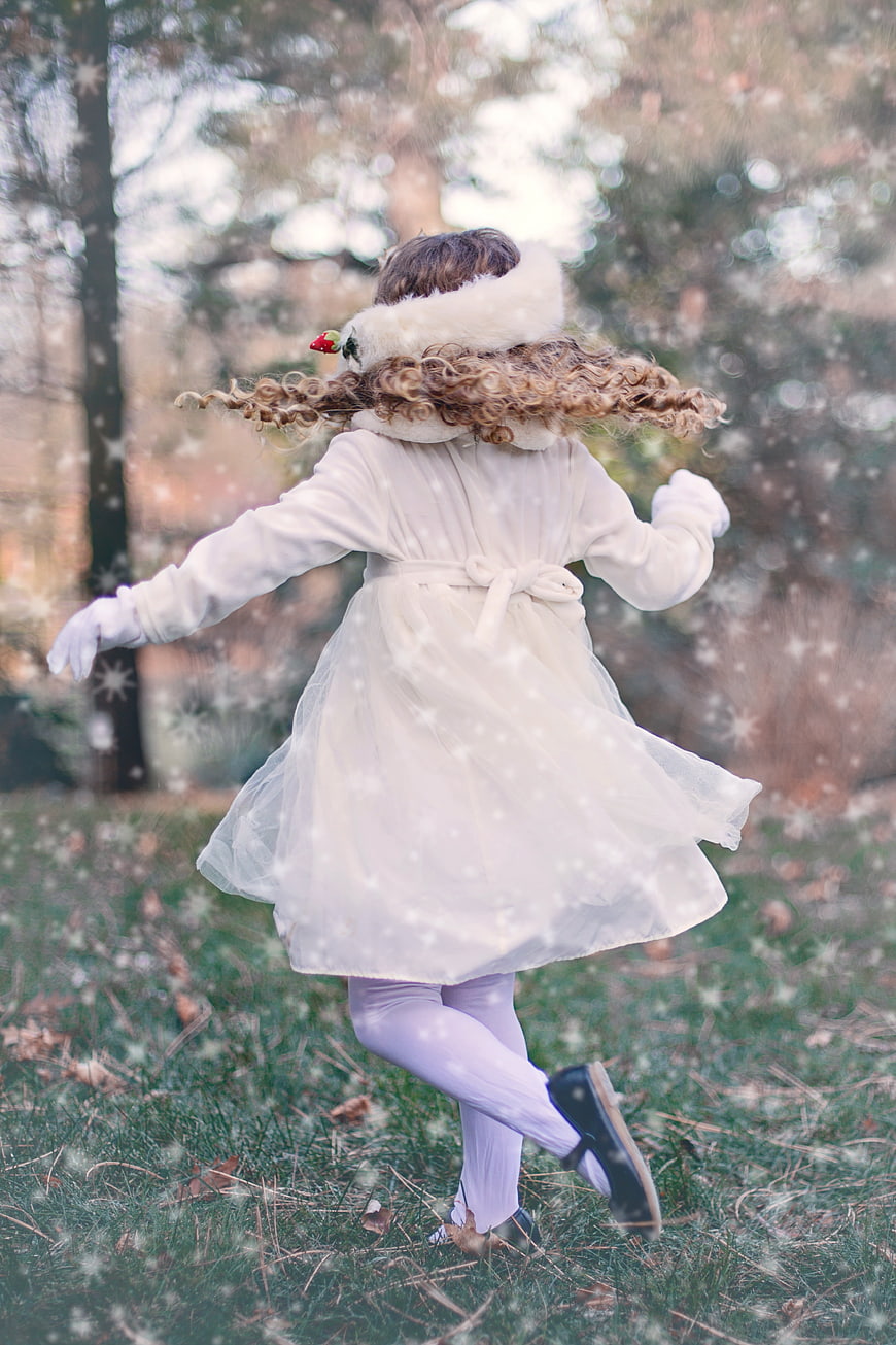 Little girl in white coat twirling in snowy winter forest