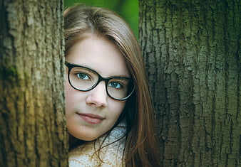 Portrait of Young Woman with Glasses Peeking from Behind Tree