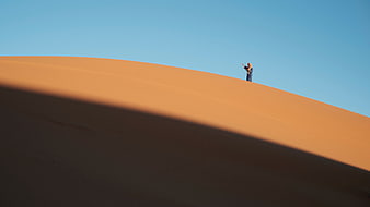 Man standing on vast orange sand dune under blue sky