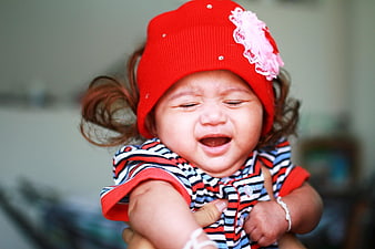 Crying baby girl wearing a red hat and striped shirt