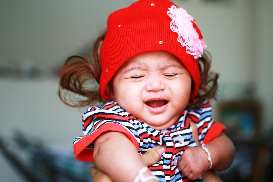 Crying baby girl wearing a red hat and striped shirt
