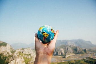 Hand holding small globe against mountain landscape