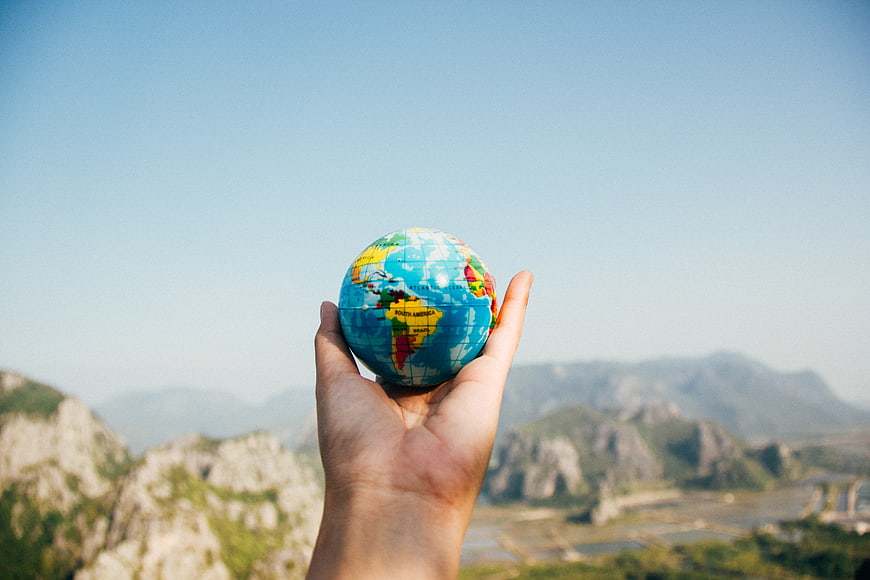 Hand holding small globe against mountain landscape