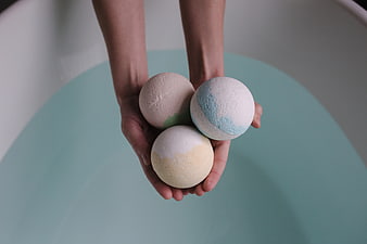 Hands Holding Three Colorful Bath Bombs Over Blue Water
