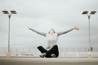 Woman sitting on pier with arms outstretched in freedom