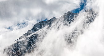 Snowy mountain peak emerging through thick clouds and fog