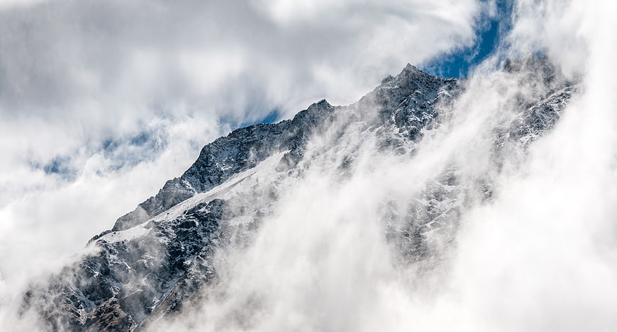 Snowy mountain peak emerging through thick clouds and fog