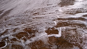 Foamy ocean waves washing over wet brown sand texture