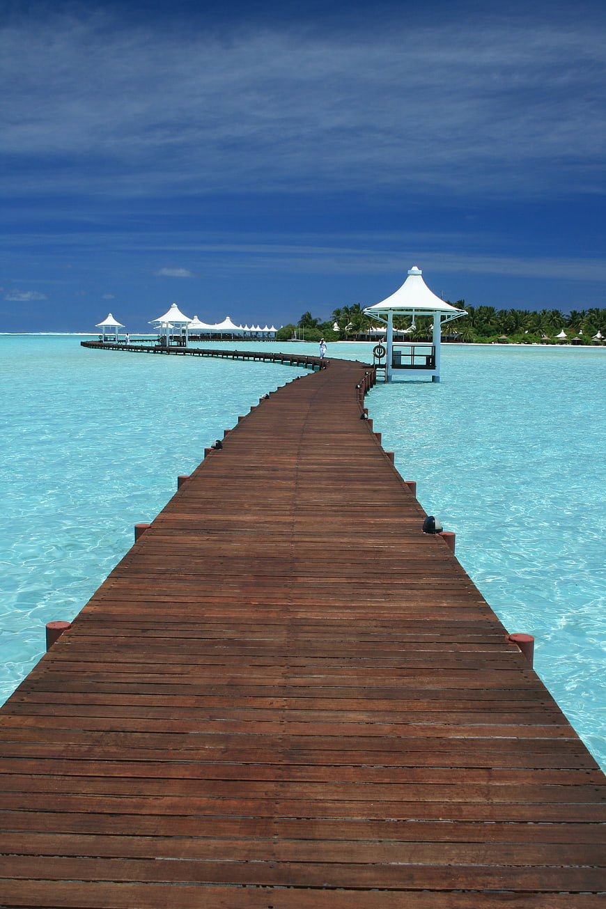 Tropical Wooden Pier Leading To Maldives Resort Over Turquoise Lagoon