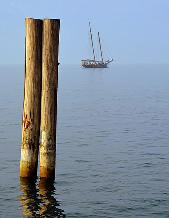 Wooden mooring posts with distant sailing ship on calm water