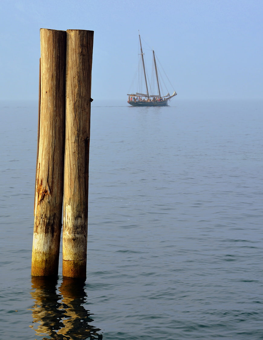 Wooden mooring posts with distant sailing ship on calm water