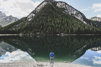 Man standing by mountain lake with perfect reflection