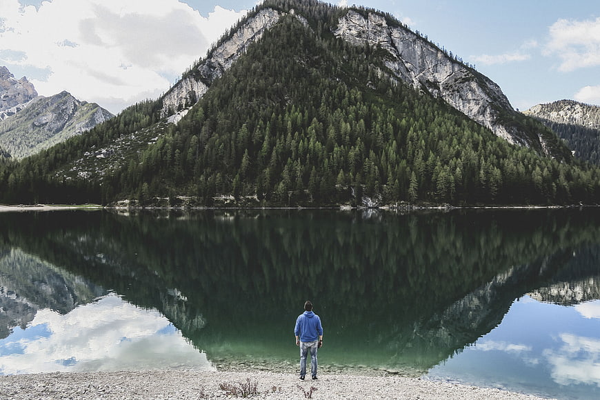 Man standing by mountain lake with perfect reflection