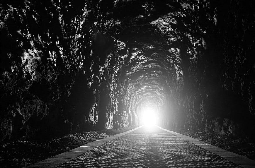 Black and white view of a dark tunnel with bright light at the end