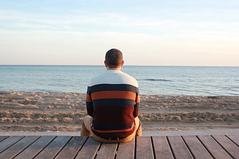 Man Sitting on Wooden Deck Looking Out at Calm Ocean