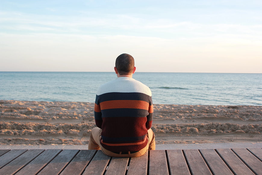 Man Sitting on Wooden Deck Looking Out at Calm Ocean