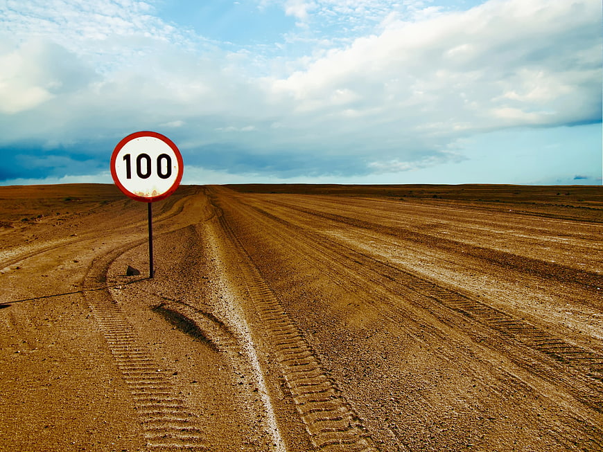 Speed limit sign 100 on dusty desert road
