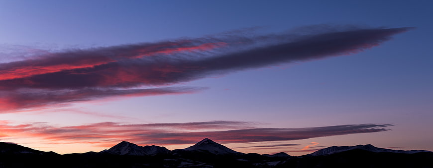 Dramatic sunset over snow-capped mountain peaks with vibrant clouds