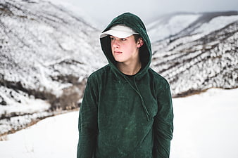 Young Man in Green Hoodie Standing in Snowy Mountains