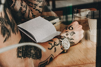 Tattooed man writing in notebook with coffee