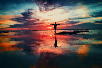 Silhouette of Man with Arms Outstretched on Beach at Sunset