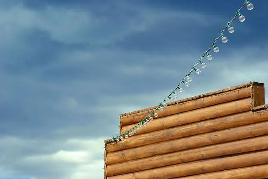 Clear String Lights on Wooden Log Wall Against Blue Sky