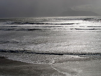Moody ocean waves on a gray beach with distant mountains