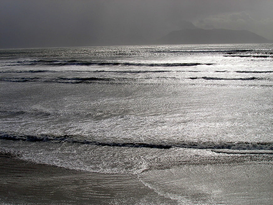Moody ocean waves on a gray beach with distant mountains