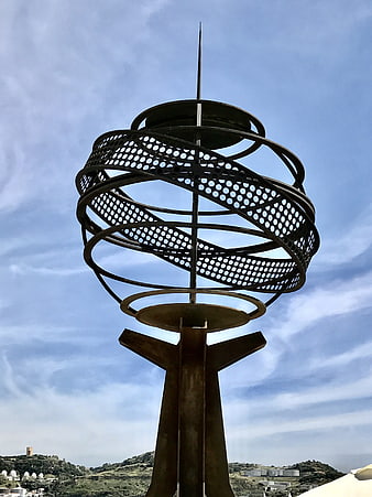 Modern metal sculpture with perforated rings against blue sky