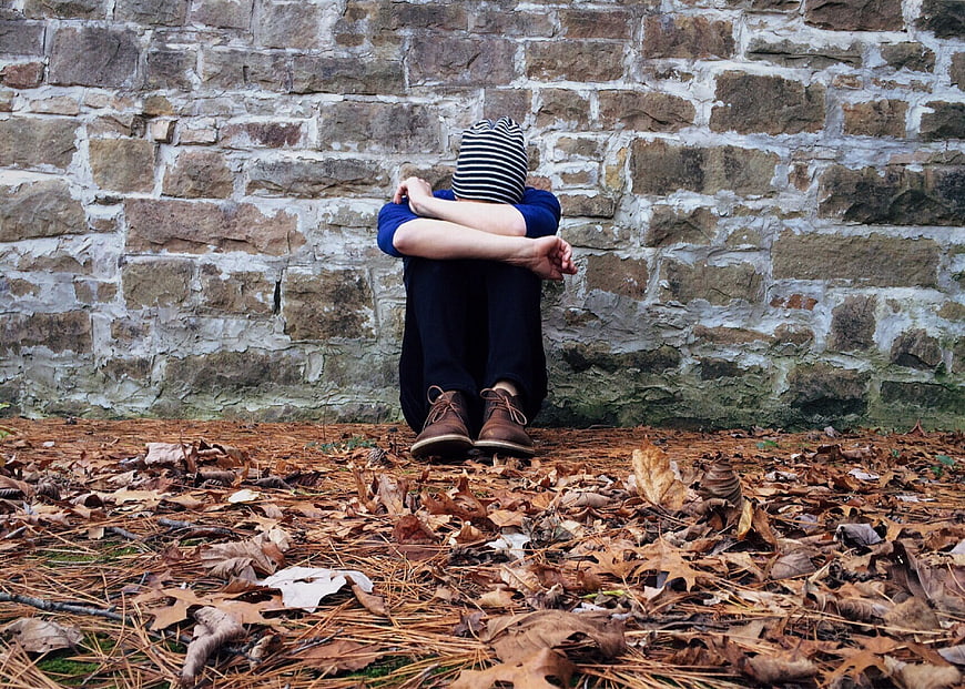 Lonely boy sitting against stone wall in autumn leaves