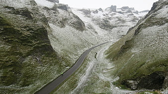 Cyclist on winding mountain road with snow and green grass