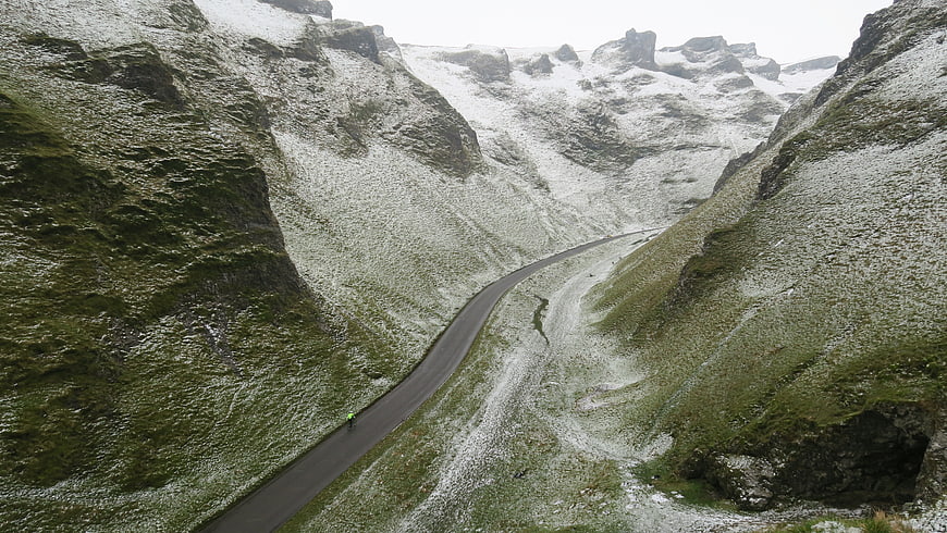Cyclist on winding mountain road with snow and green grass