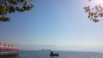 Seascape with pier, cargo ship, and mountains under blue sky
