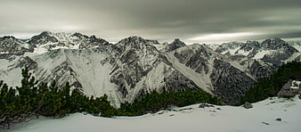 Panoramic view of snow-covered mountain peaks under cloudy sky