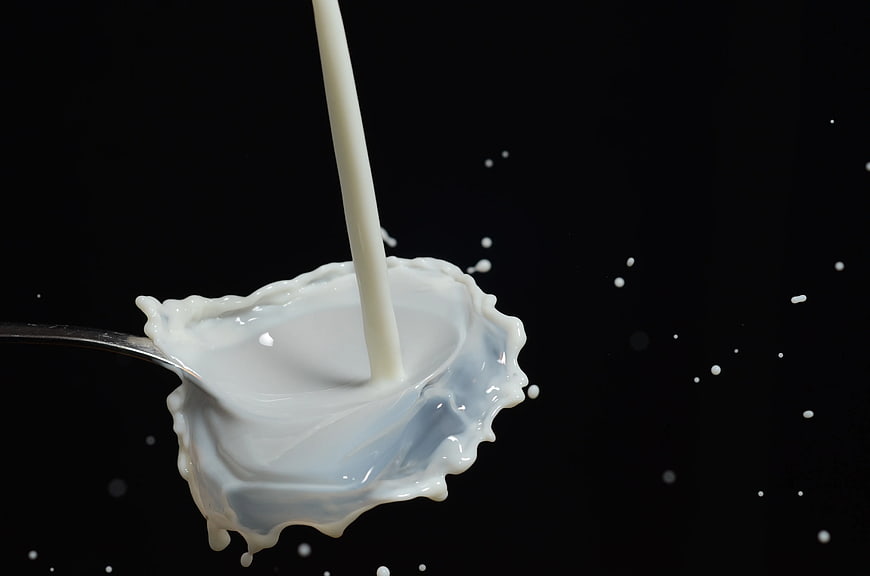 Pouring Milk Splash on Spoon Black Background