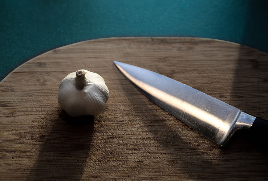 Garlic bulb and chef knife on wooden cutting board